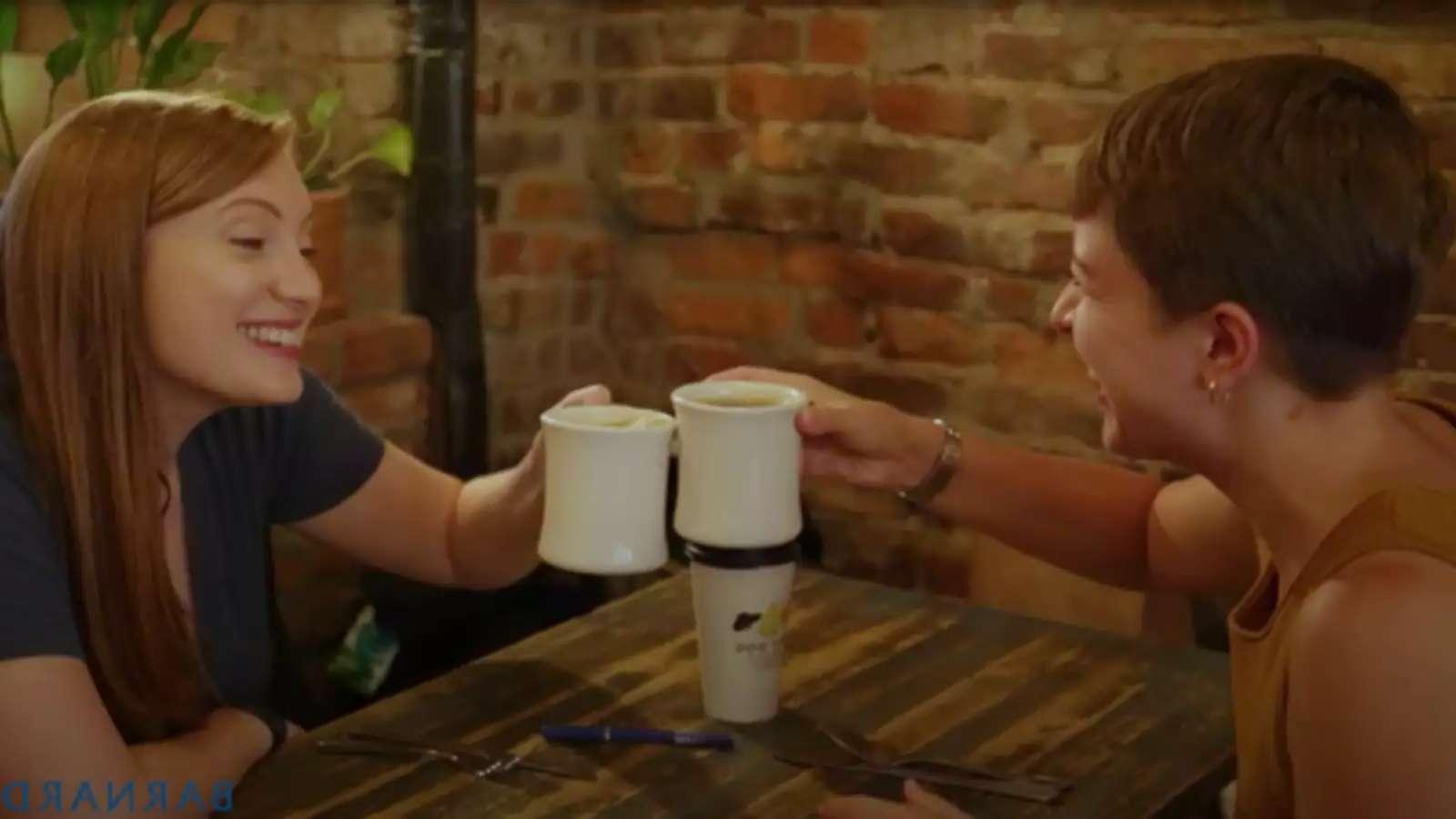 Two Barnard alums clinking coffee mugs at a wooden table in a coffee shop